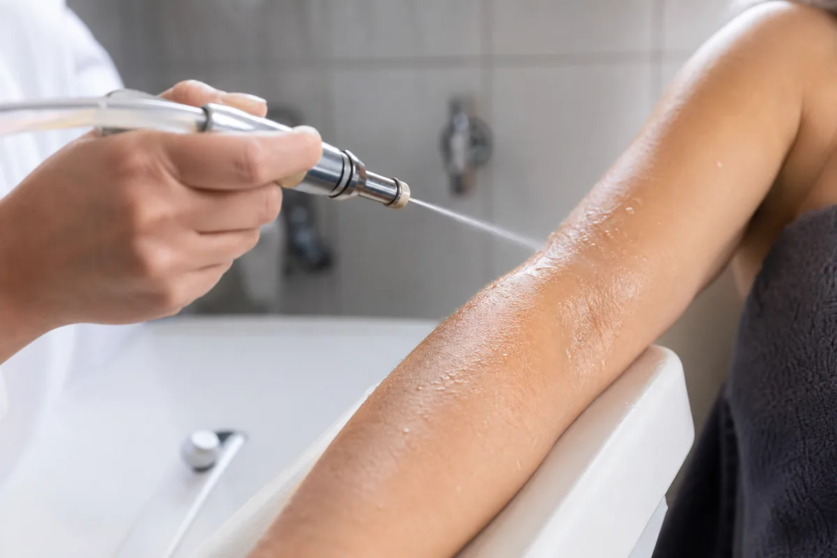 Soin par jet fin d’eau thermale appliqué sur un avant-bras dans une cabine de cure